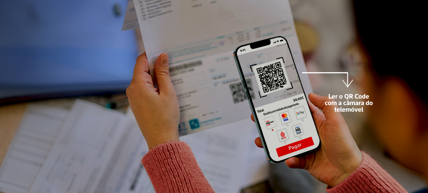 Pessoa segura uma fatura e um telemóvel com QR Code visível para pagamento digital.
