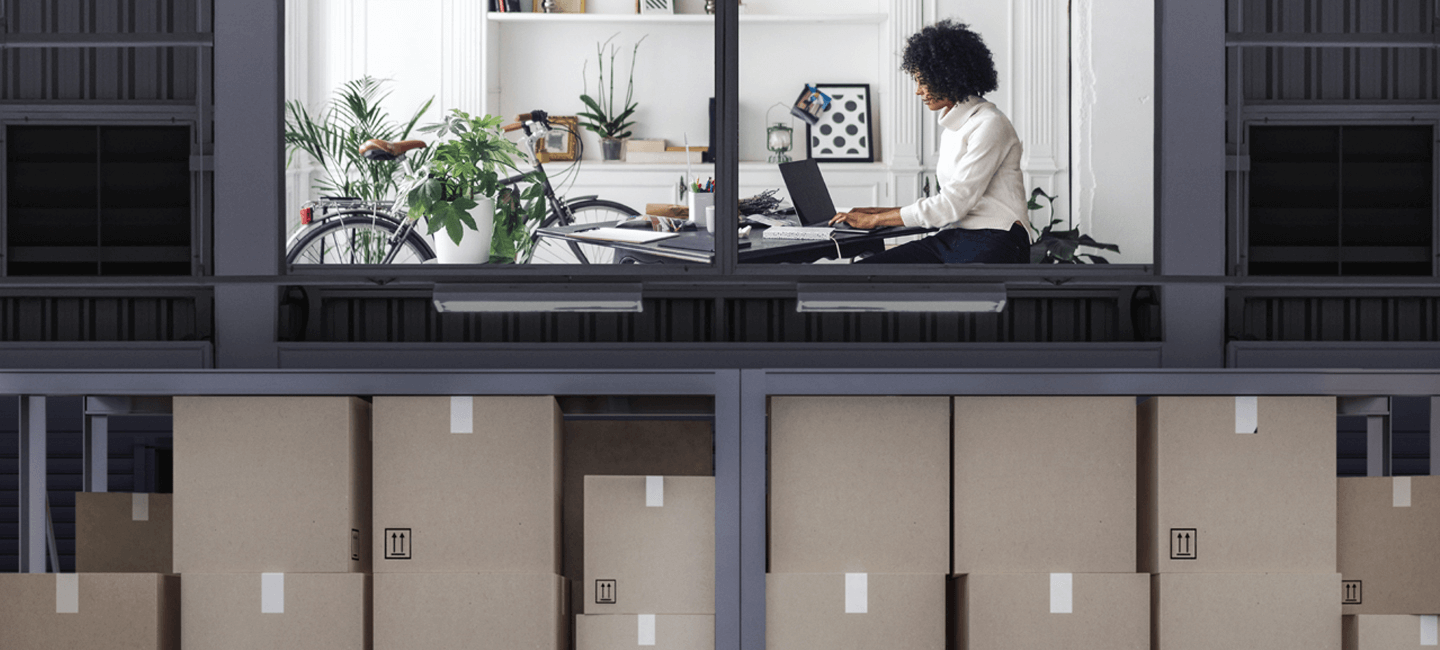 Armazém com encomendas e um escritório no andar de cima onde está uma senhora numa secratéria com computador