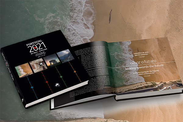 Dois livros sobre uma praia, um está fechado com título “Portugal 2021” e outro aberto com texto.